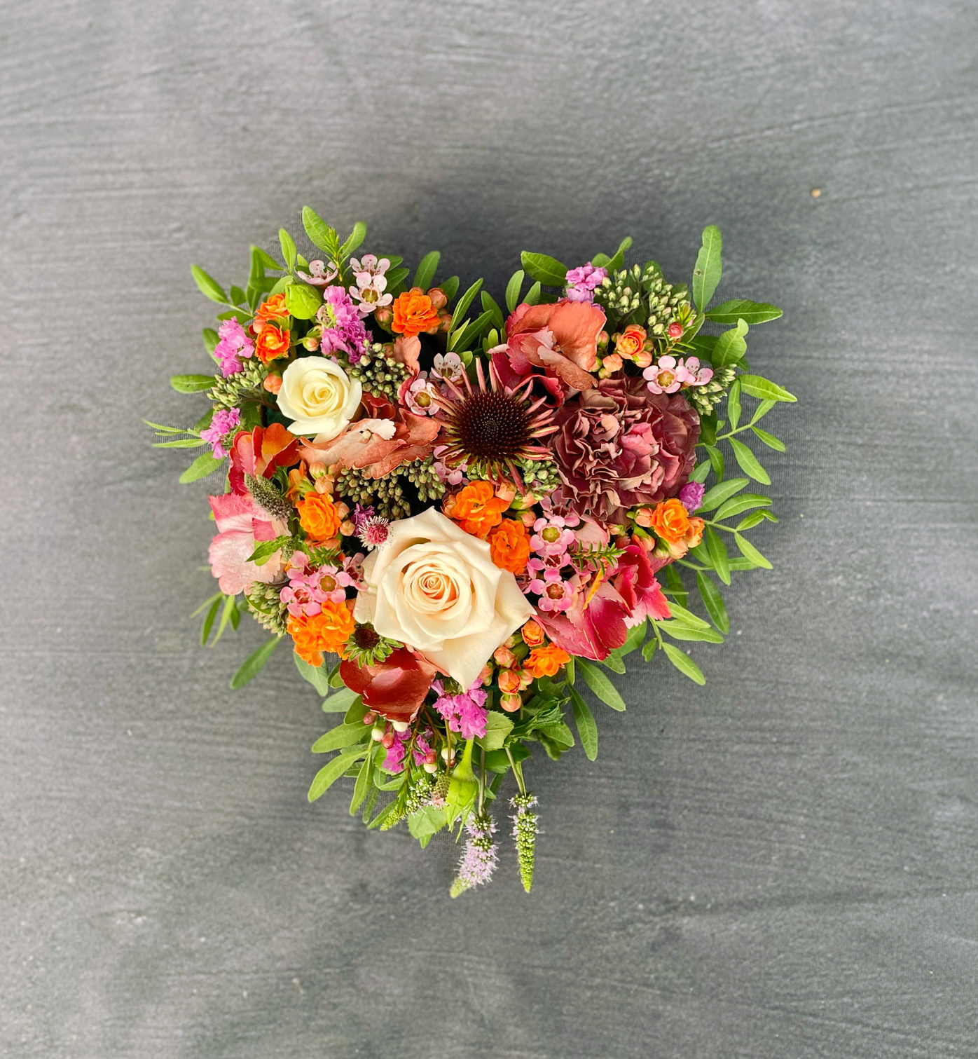 Oasis hjerte til begravelse. Hjertet er bundet med blomster i varme røde og orange nuancer. 