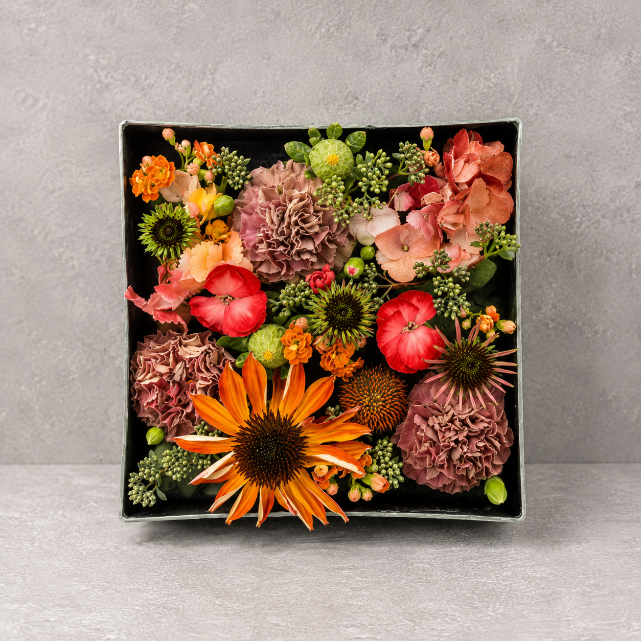 Signatur box med blomster sat tæt i en firkantet æske. Den er stukket med blomster i varme røde, orange og grønne farver.  