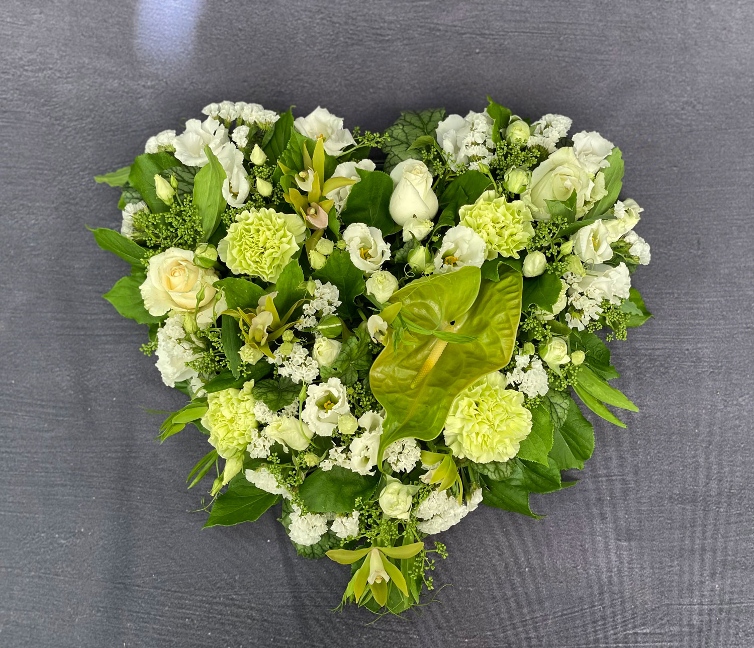 Oasis hjerte til begravelse. Hjertet er bundet med blomster i hvide nuancer og et strejf af vinter. 