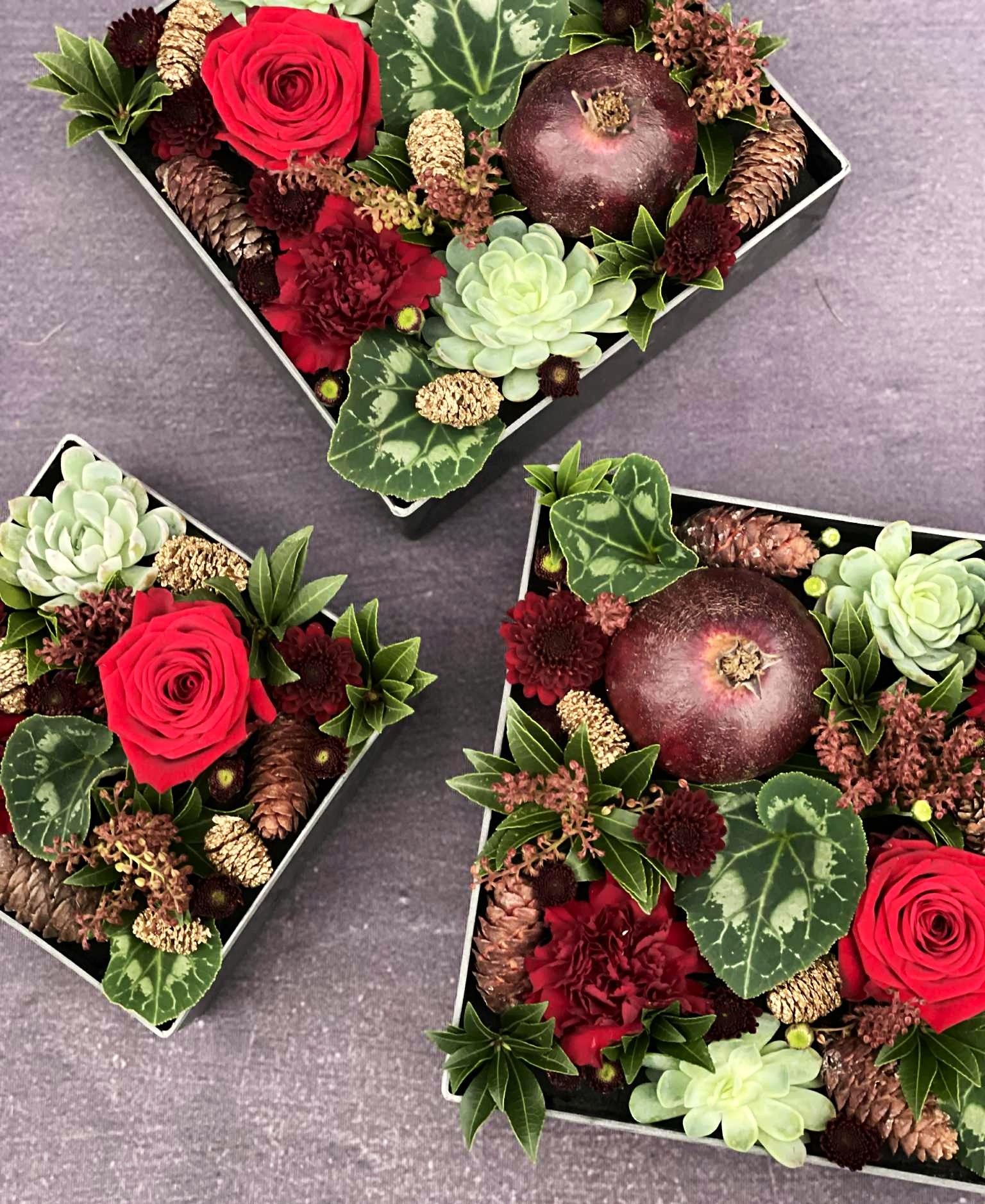Tre firkantede boxe stukket med kogler, røde roser, husløg og granatæbler. 