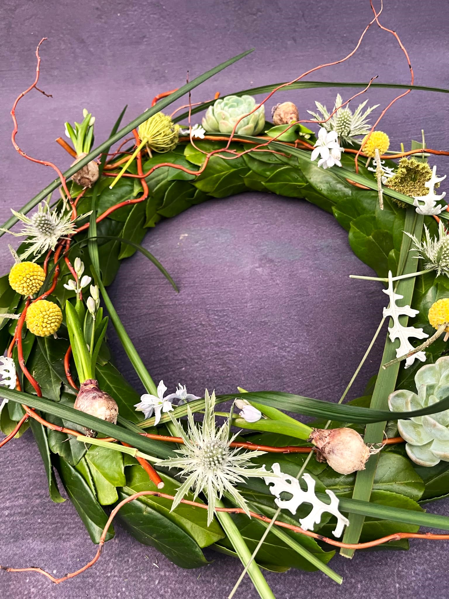 Krans med bund af grønne blade, mandstro, gule blomster og hyacinter.