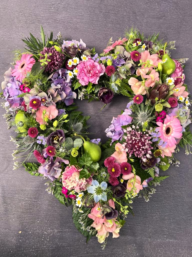 Åbent oasis hjerte med årstidens friske blomster. 