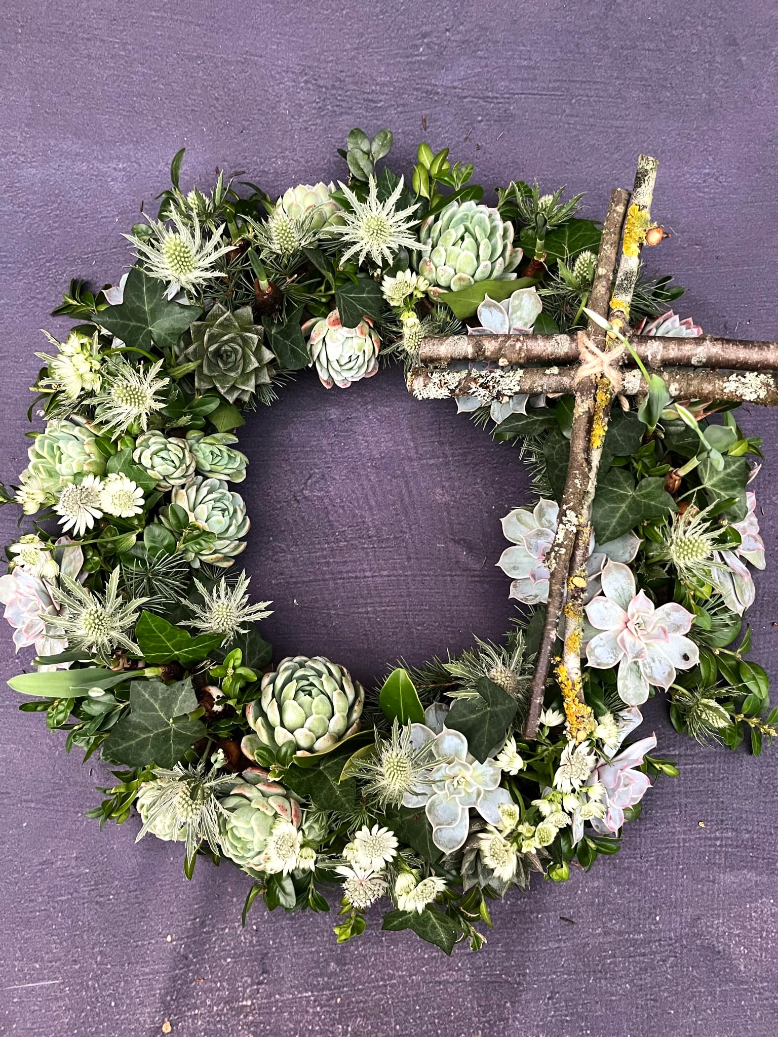 Krans med i grønne nuancer, med echeveria, mandstro og et kors af kviste. 