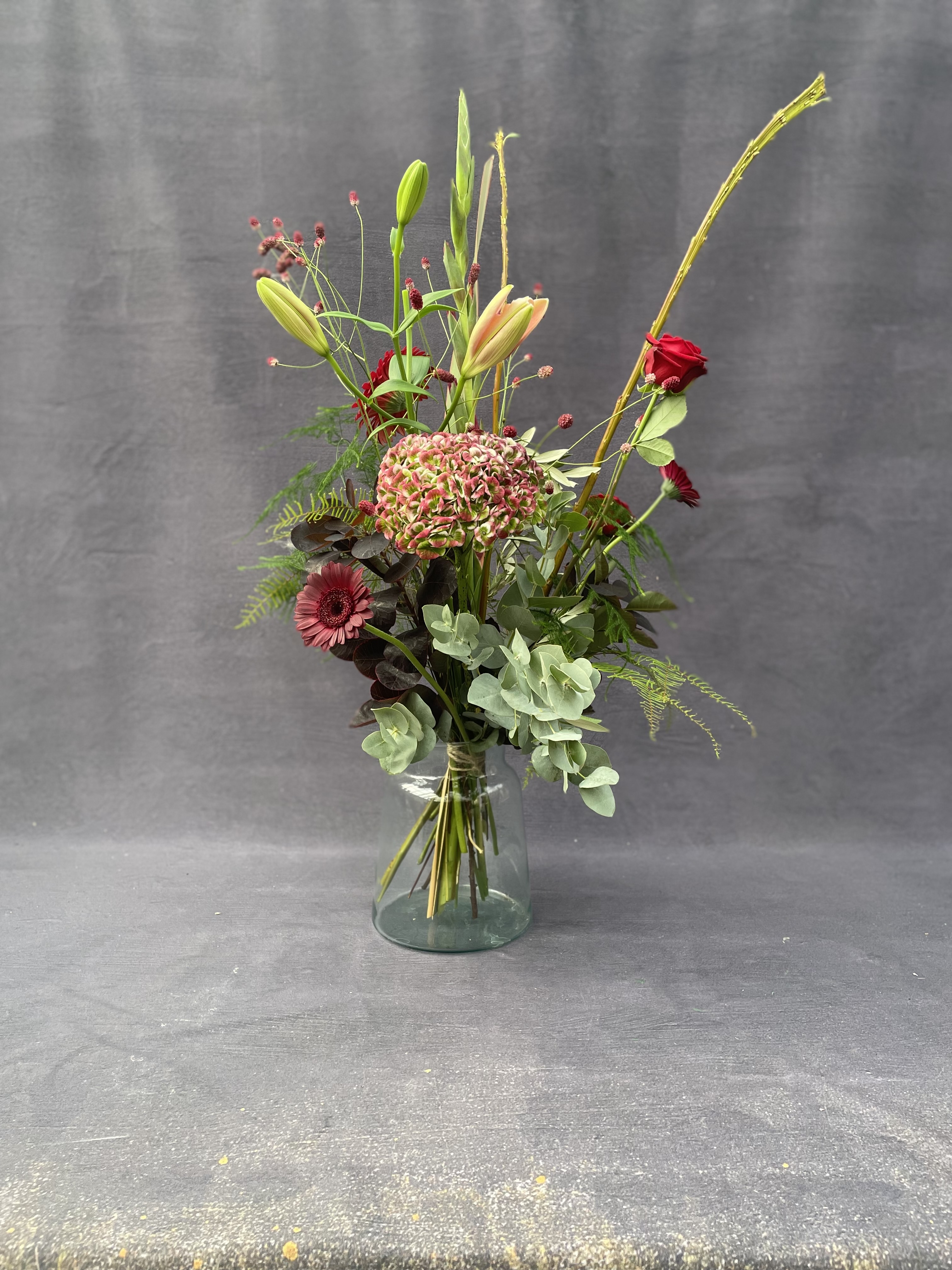 Vild og høj julebuket med hortensia, roser, amaryllis og grønne materialer. 