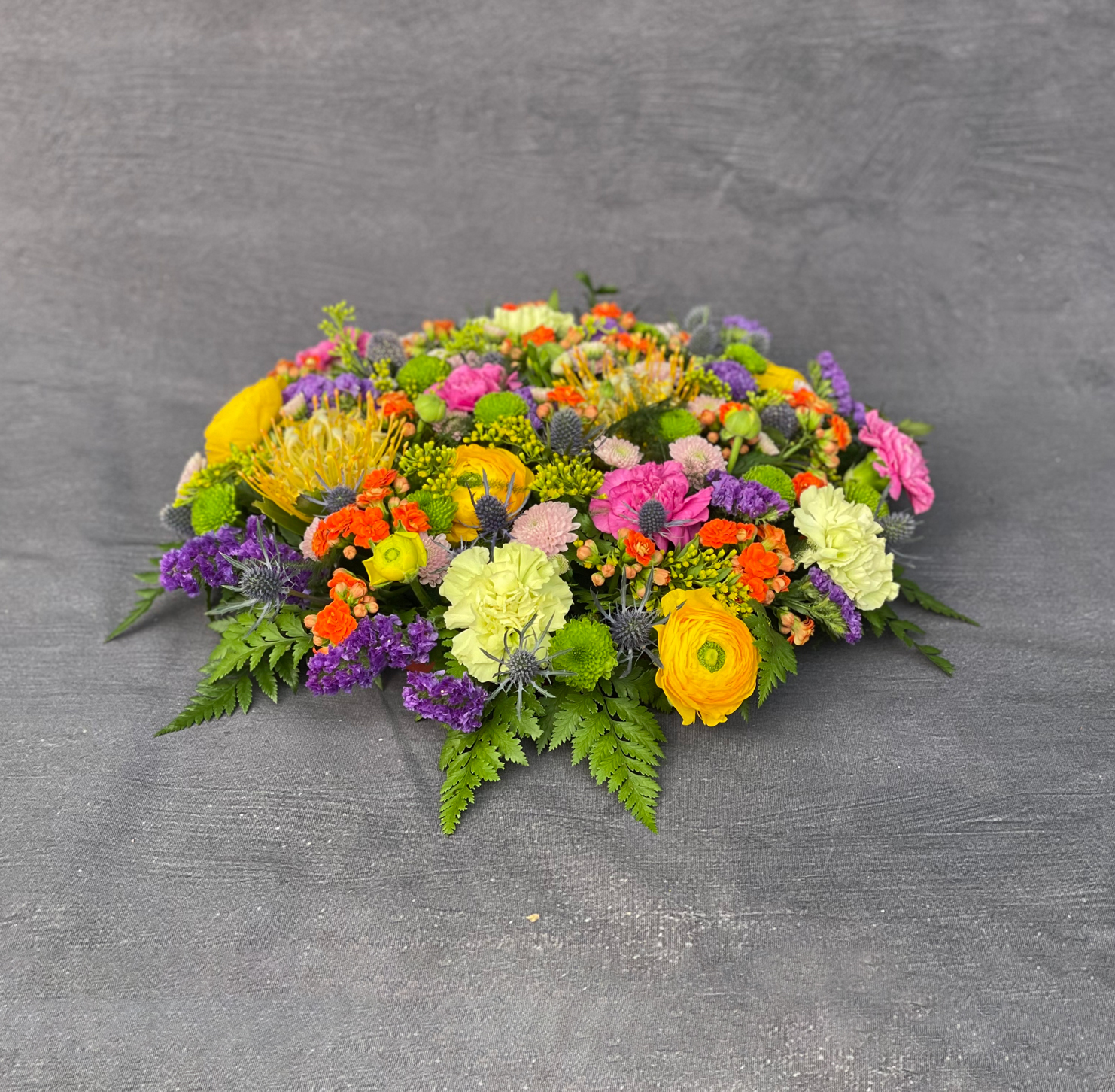 Begravelsespude bundet med blomster i stærke multifarver hos Acacia Blomsterkunst. 